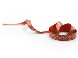 Elegante nastro rosso con piccolo motivo geometrico bianco. Nastro bifacciale, ideale per decorazioni natalizie B2B. Produttore AMGS Group.